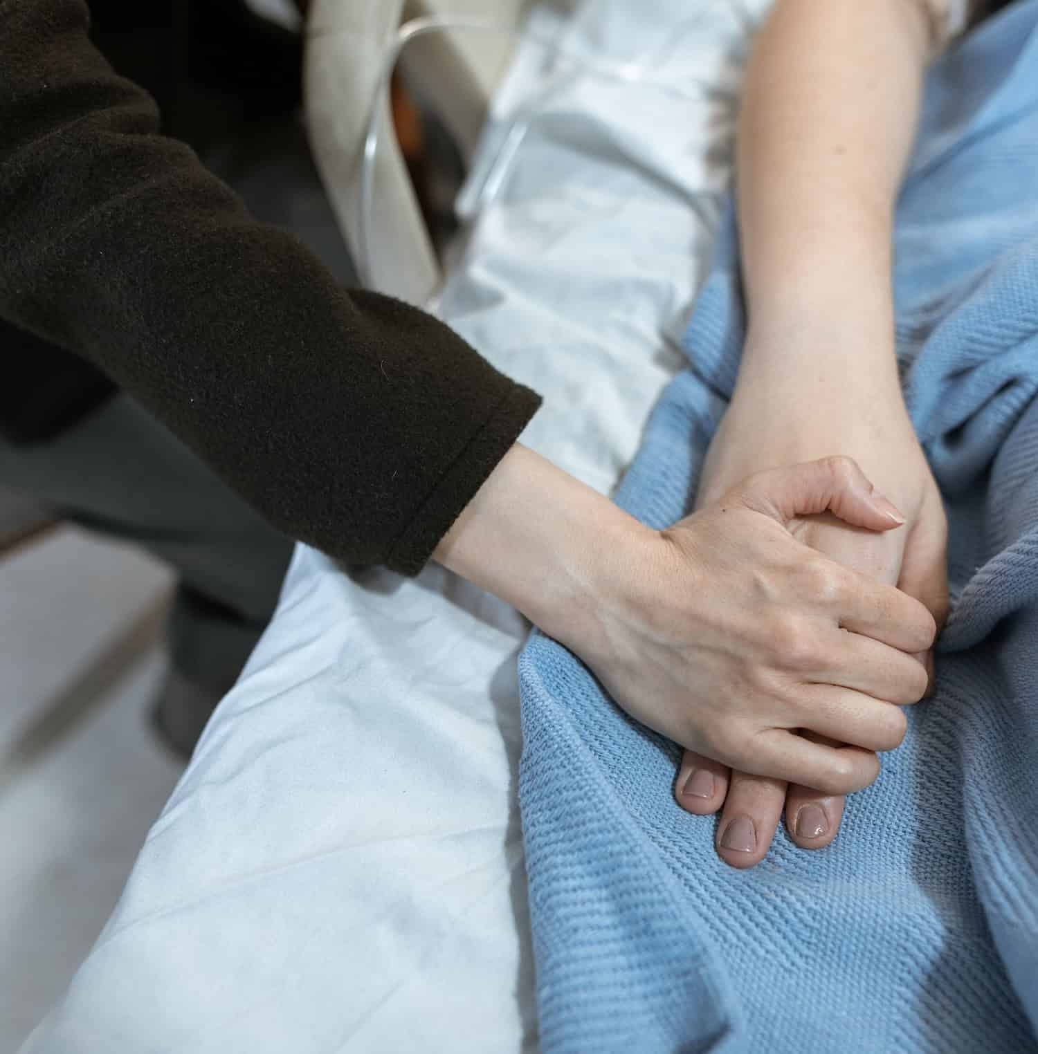 patient's hand being held in hospital bed